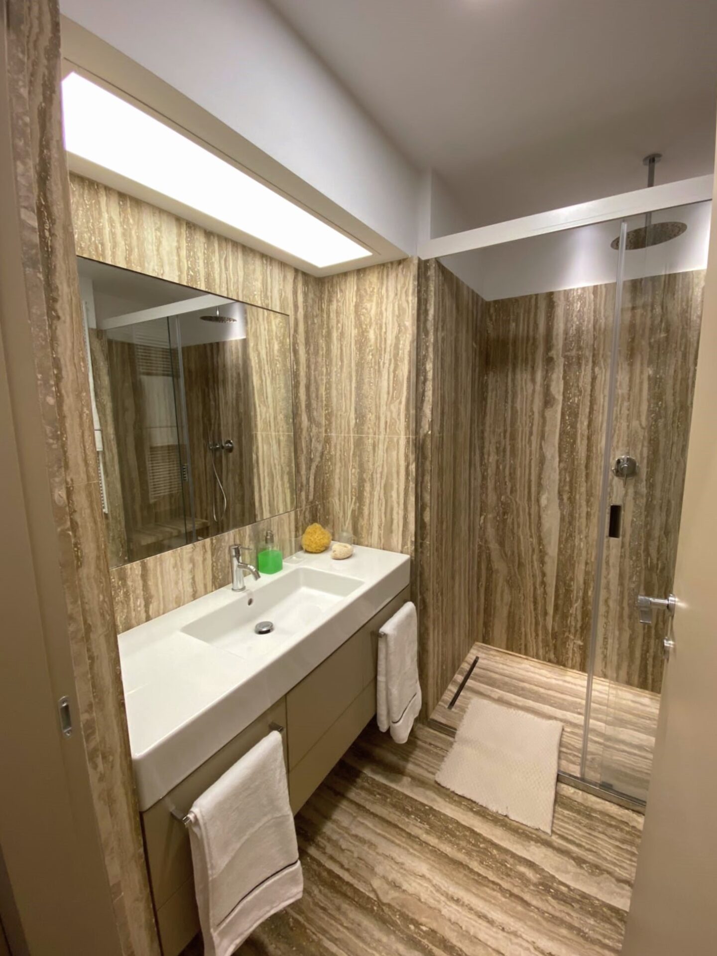 Il bagno rivestito in Travertino Noce con mobile sospeso e doccia