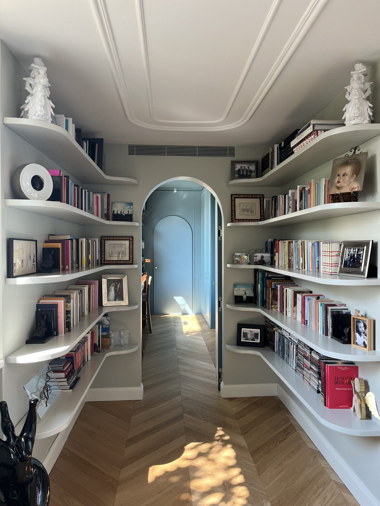 Libreria con mensole sagomate a parete ai lati di un passaggio ad arco