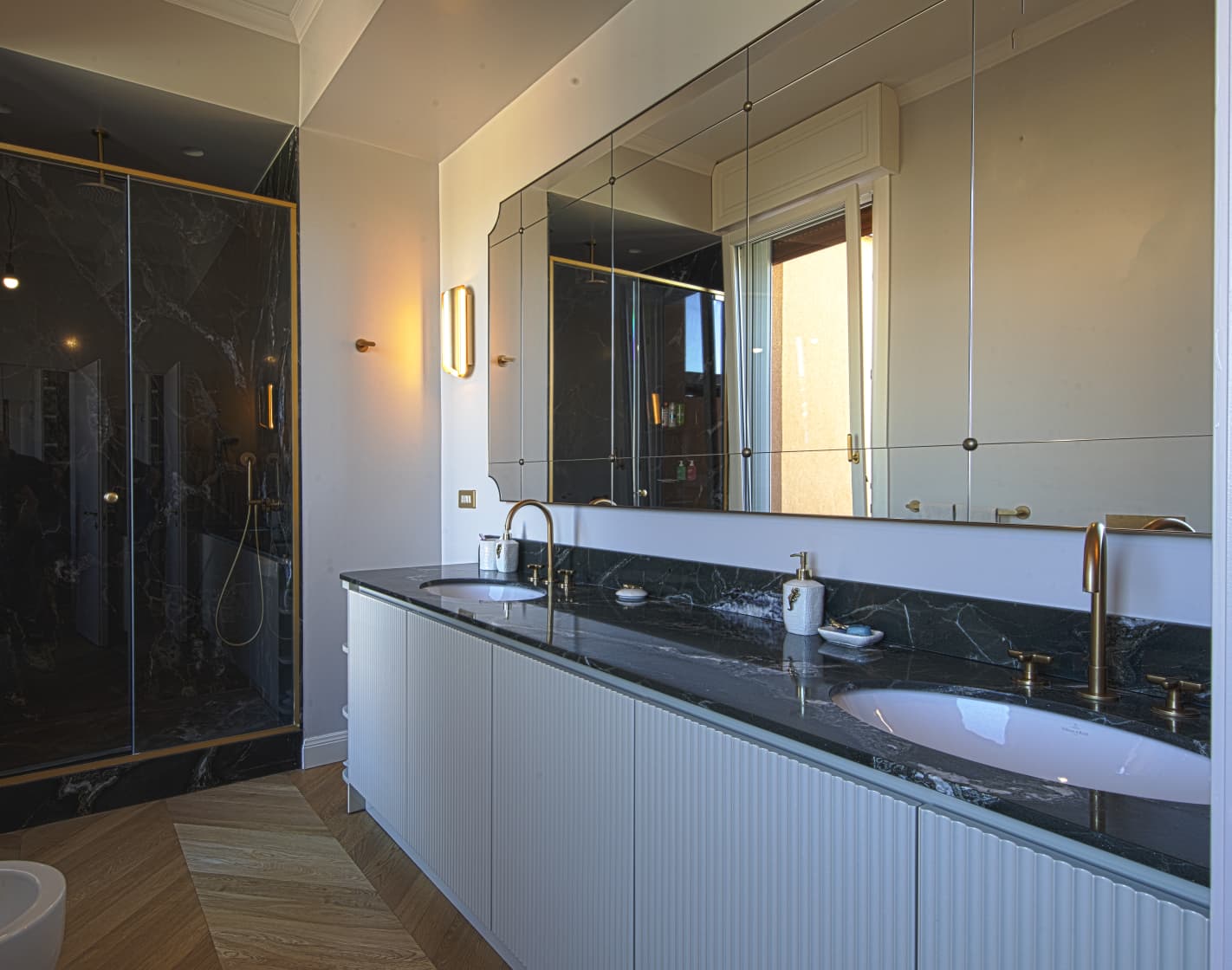 Il mobile lavabo con piano scuro e lo specchio su misura a tutta larghezza